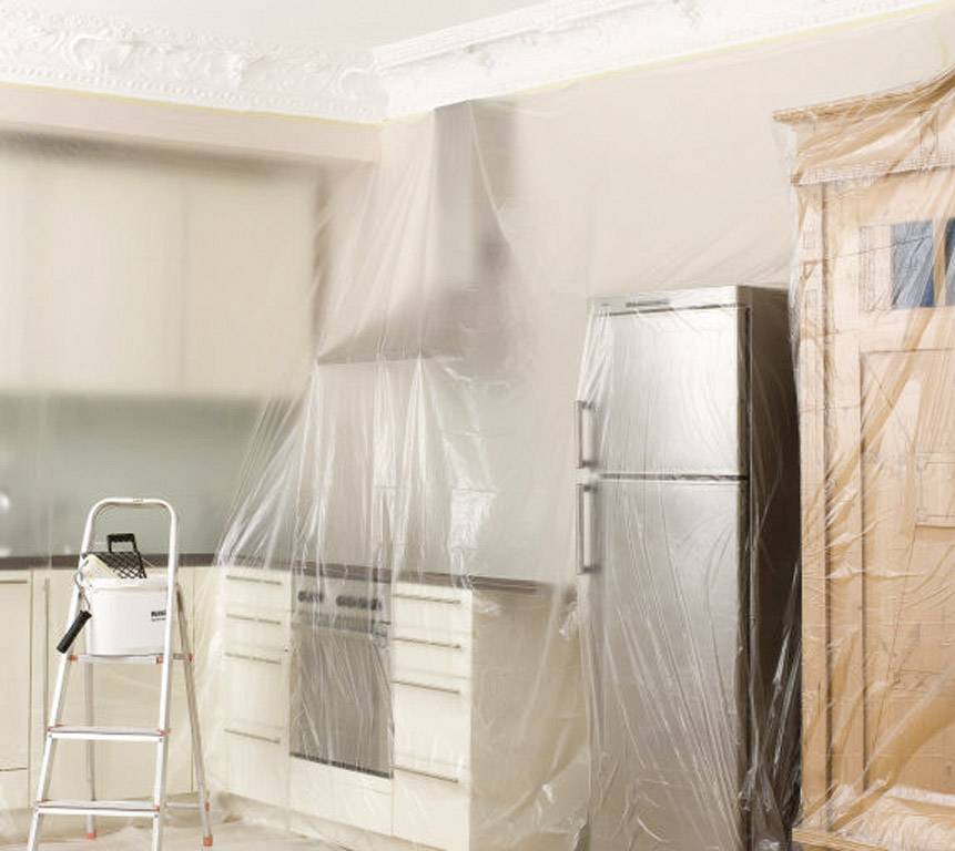 Kitchen prepared for painting: Furniture and appliances covered with plastic sheeting, ladder in place.