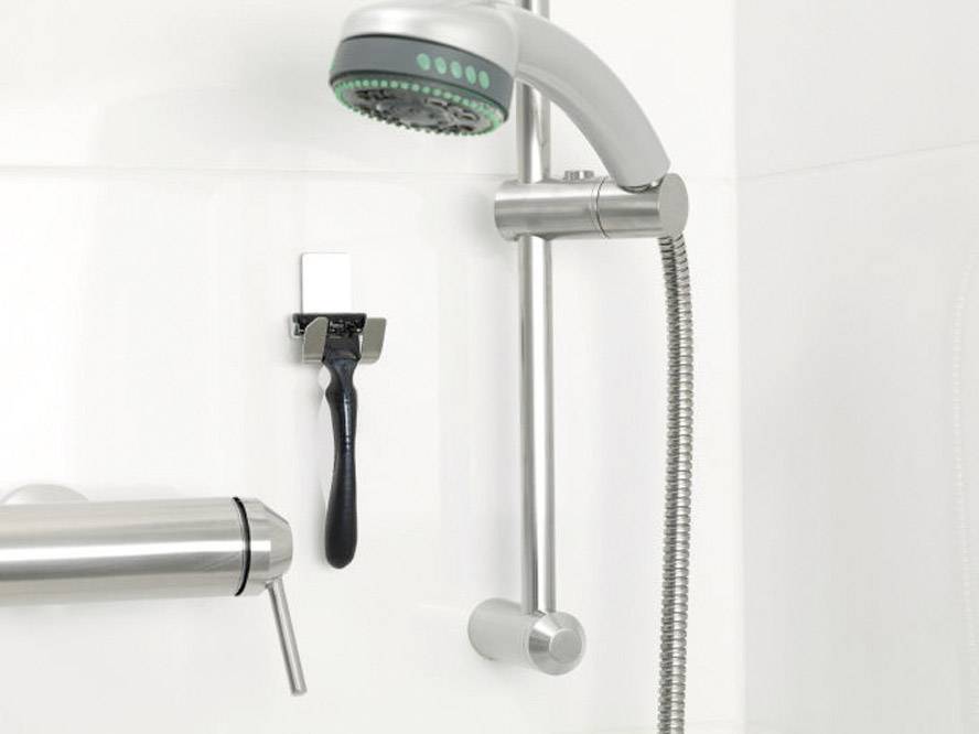 A shower with a shower head and holder, with a razor attached to a hook on the white wall beside it.