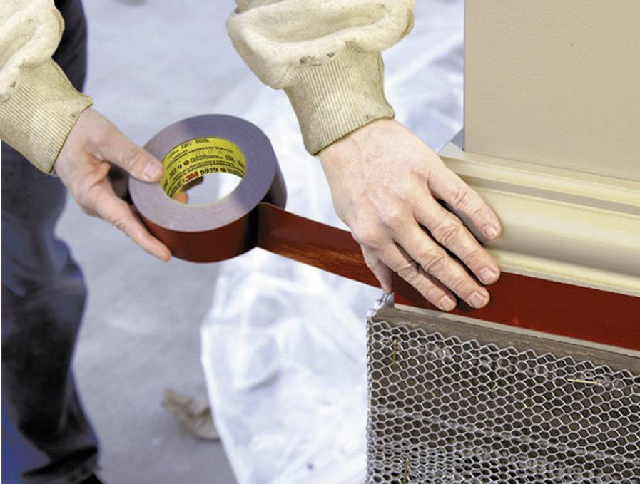 'A person is sticking a red ribbon around a column. Hands are holding the ribbon firmly. The background shows blurry construction equipment.'