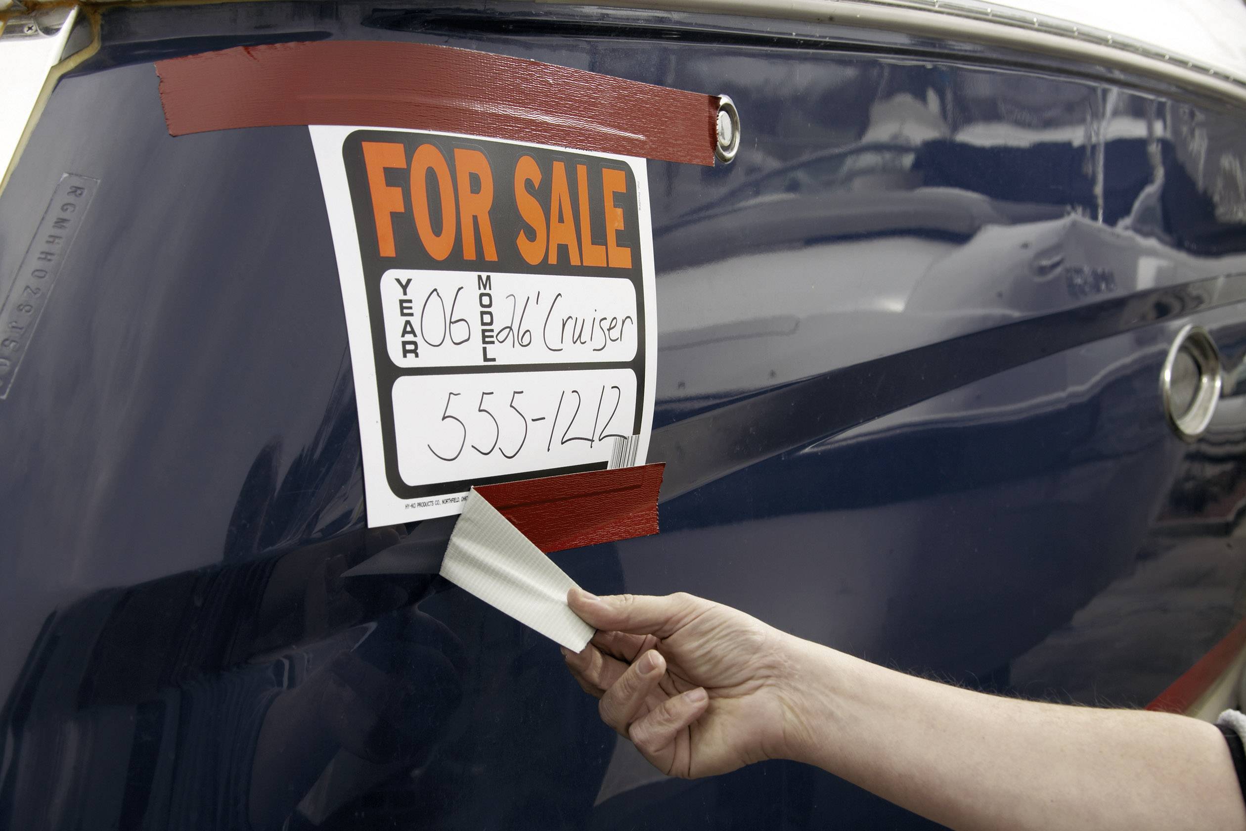 Boat for sale with a sign '60s Model Cruiser, 555-1242'. A hand removes an old sticker.