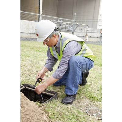 A worker wearing a hard hat and high-visibility vest is examining a cable box in the ground. A fence is visible in the background.
