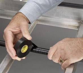 A person is wrapping a black cable with electrical tape. They are holding the tape with both hands and wearing a gold ring on their right hand.