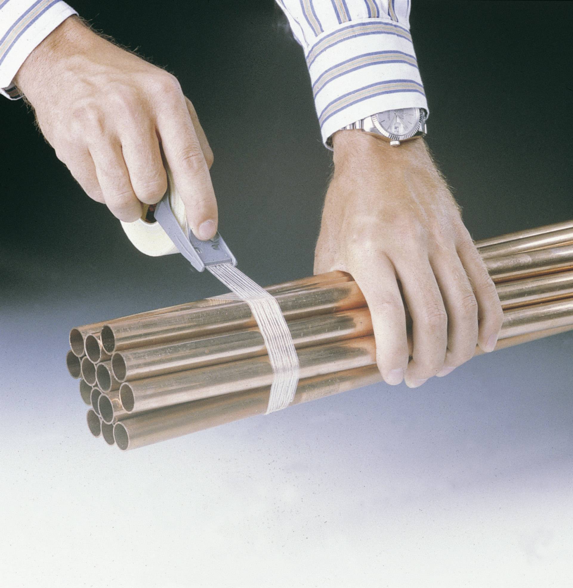 A person is cutting plastic banding from a bundle of copper pipes using a utility knife. Focus on hands and pipes.