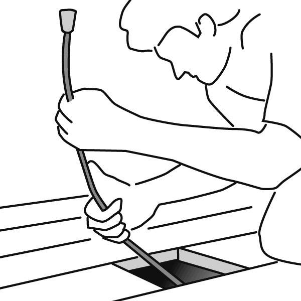 A person is kneeling and threading a cable through a small rectangular slot in the floor.