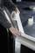 A person is sticking a roll of transparent adhesive tape along the edge of a metal surface, possibly for protection or sealing purposes.