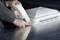 Hands of a person are applying a white sealing tape to a silver metal surface in order to attach a white plastic cover.