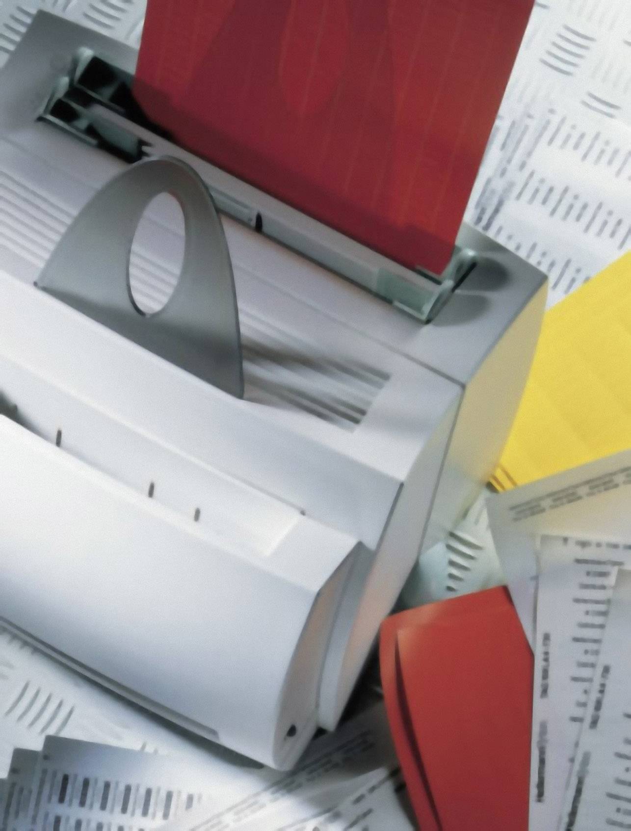 A stack of paper is being shredded by a document shredder. Red and yellow sheets are scattered around the device.