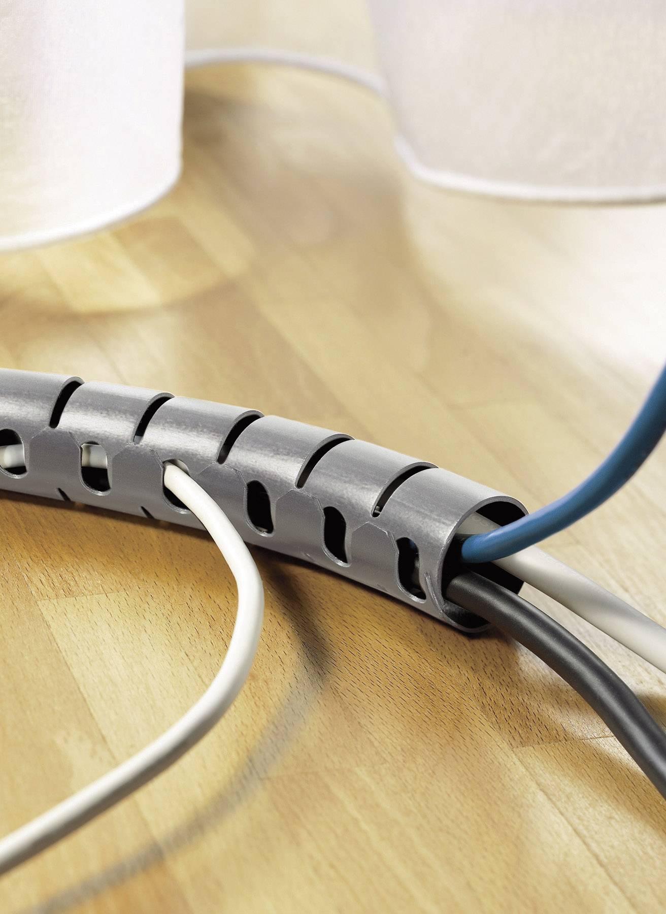 Cable management system on a wooden table: A grey cable sleeve organises white, black, and blue cables.