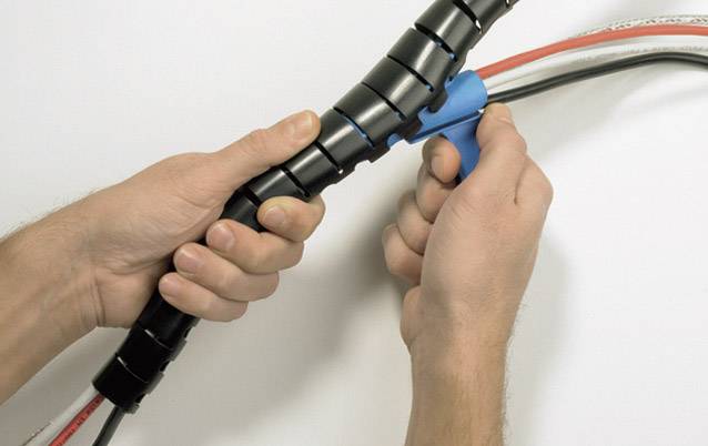 'Two hands are using a blue tool to organise cables in a black cable protection sleeve.'
