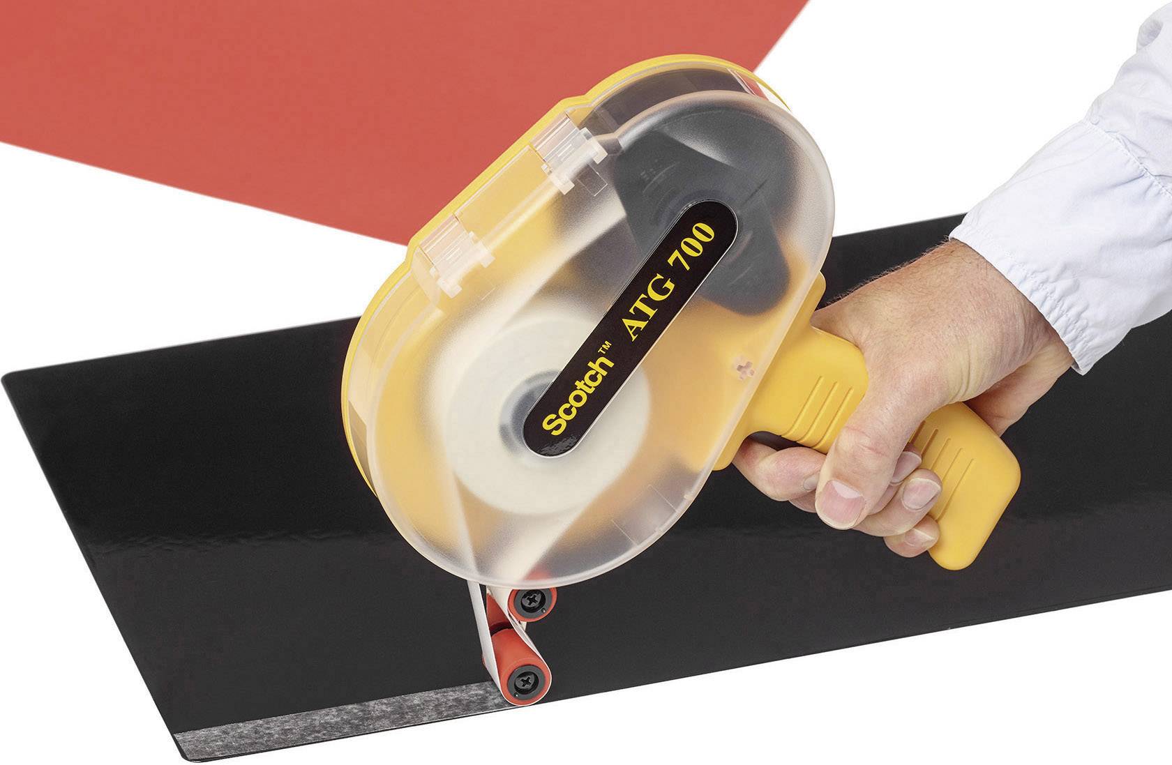 A hand is holding a Scotch ATG 700 tape dispenser. The dispenser is being applied to a black surface.