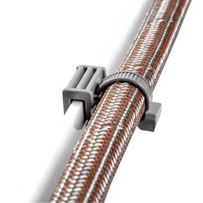 Hose clip secures a braided hose to a pipe. The clamp is made of grey plastic and is tightly fastened.