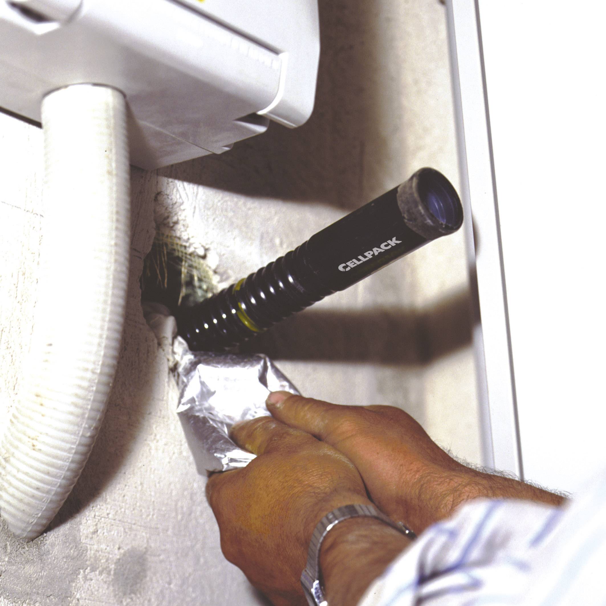 A person is using a tool to repair a hole in a wall near a pipe. It appears to be a piece of manual craftsmanship.