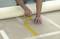 A person is placing yellow adhesive tape parallel to each other on a floor, presumably in preparation for painting or renovation work.