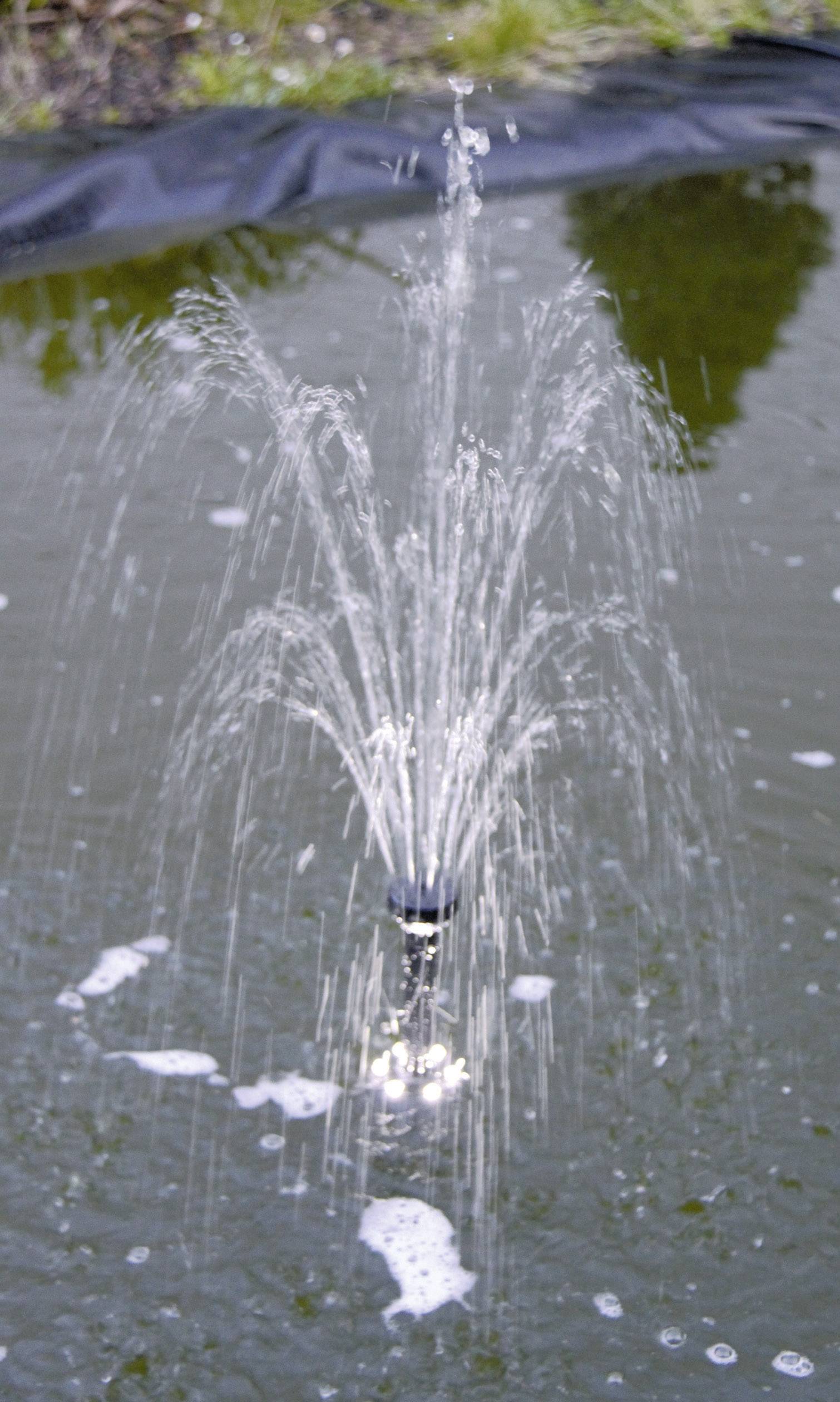 Fountain in the pond sprays water jets into the air. Background with water surface, foam and grass along the shoreline.