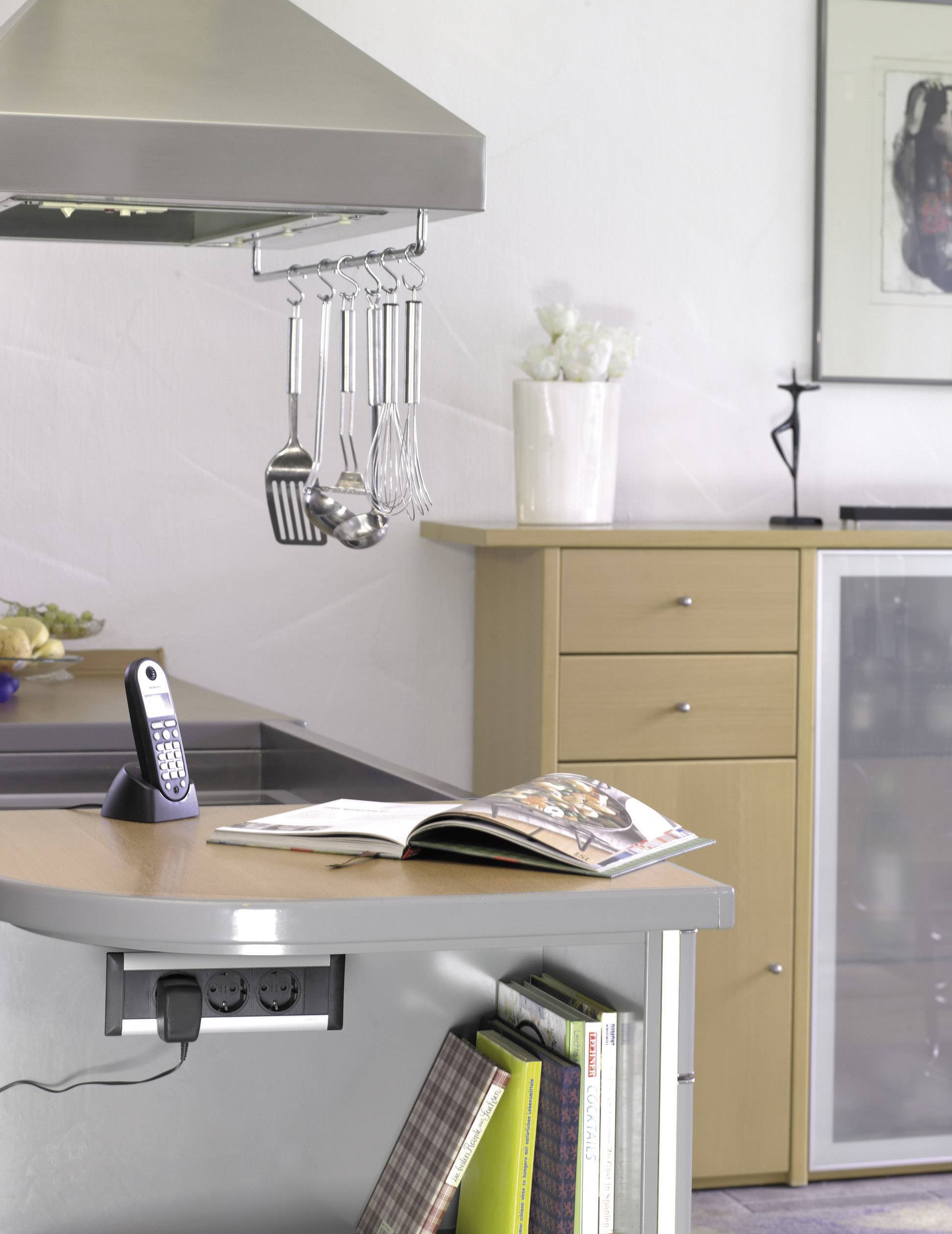A modern kitchen with hanging utensils, an open cookbook on the worktop and a cordless telephone. In the background, a sideboard.