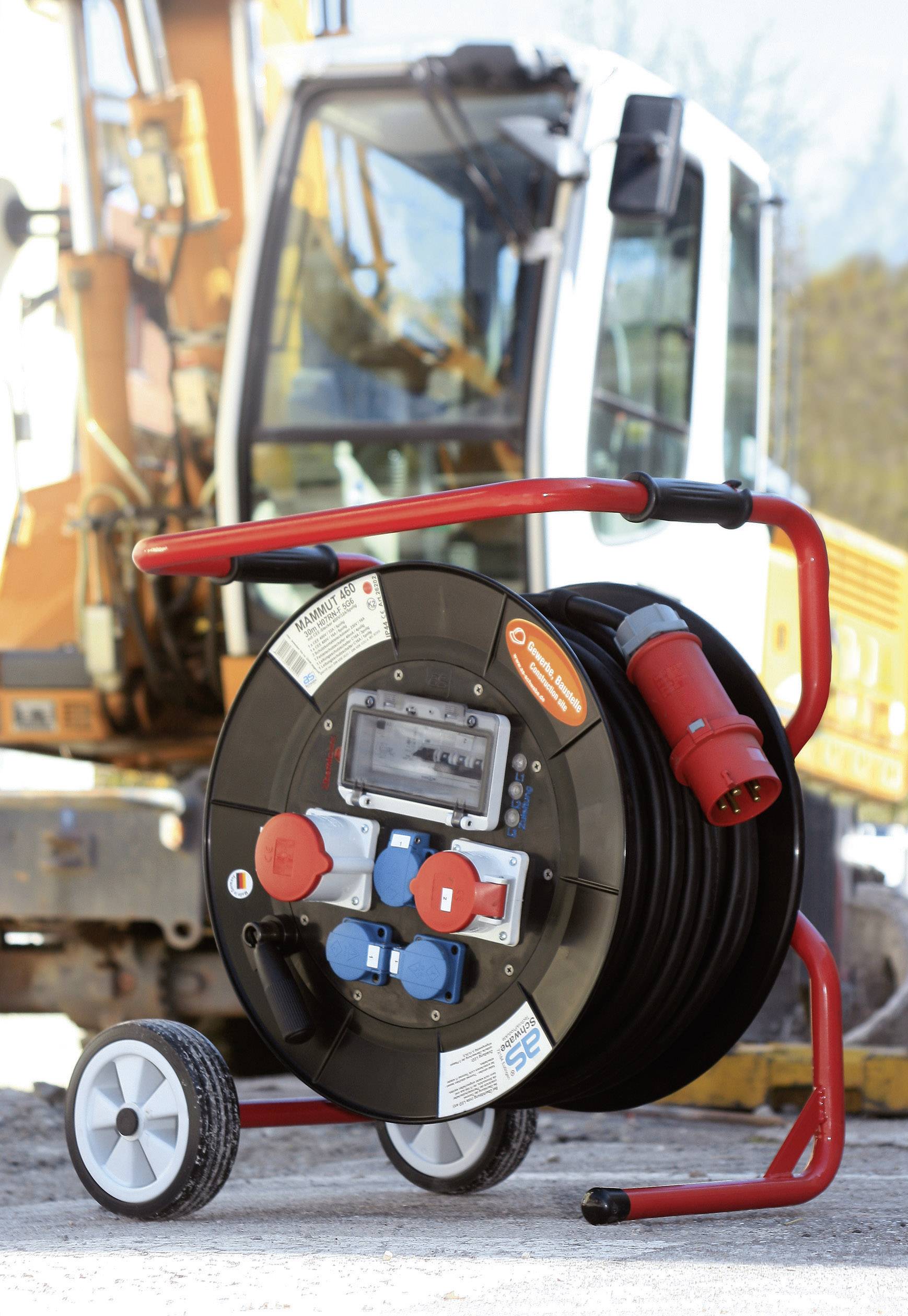 Construction site extension cable reel with carry handle and power sockets. Blurred construction machinery in the background.