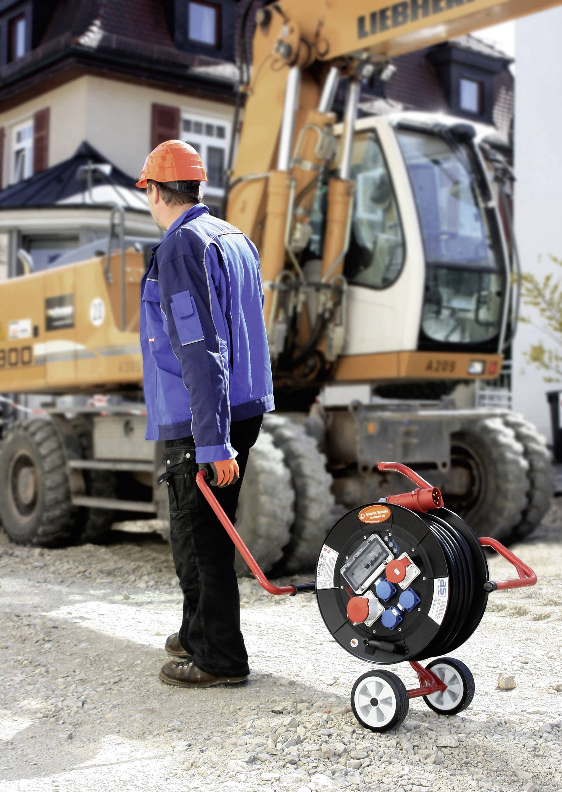 A person in workwear is pulling a cable drum behind them on a construction site. A digger can be seen in the background.