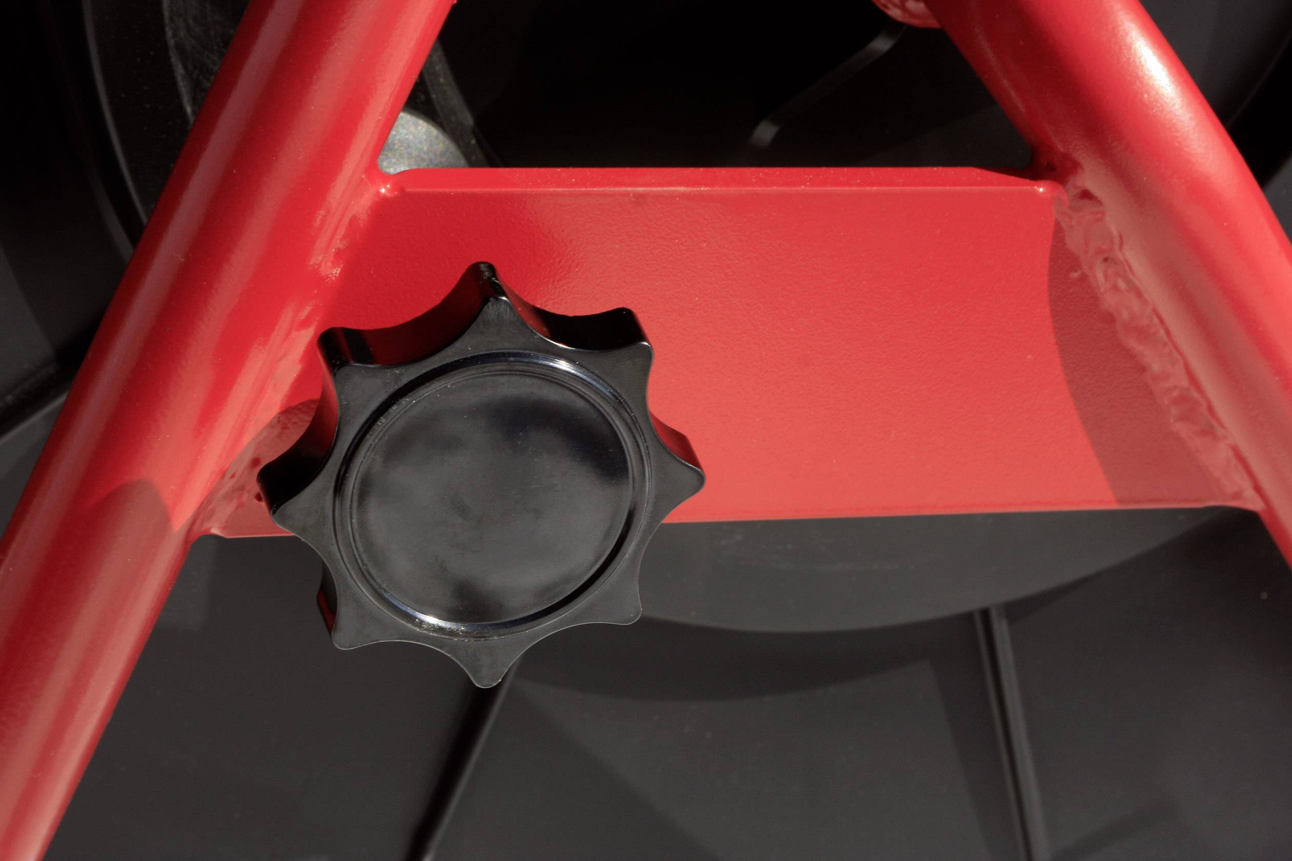Close-up of a red metal frame with a black rotary knob at its centre. The image reveals the mechanism and structure.