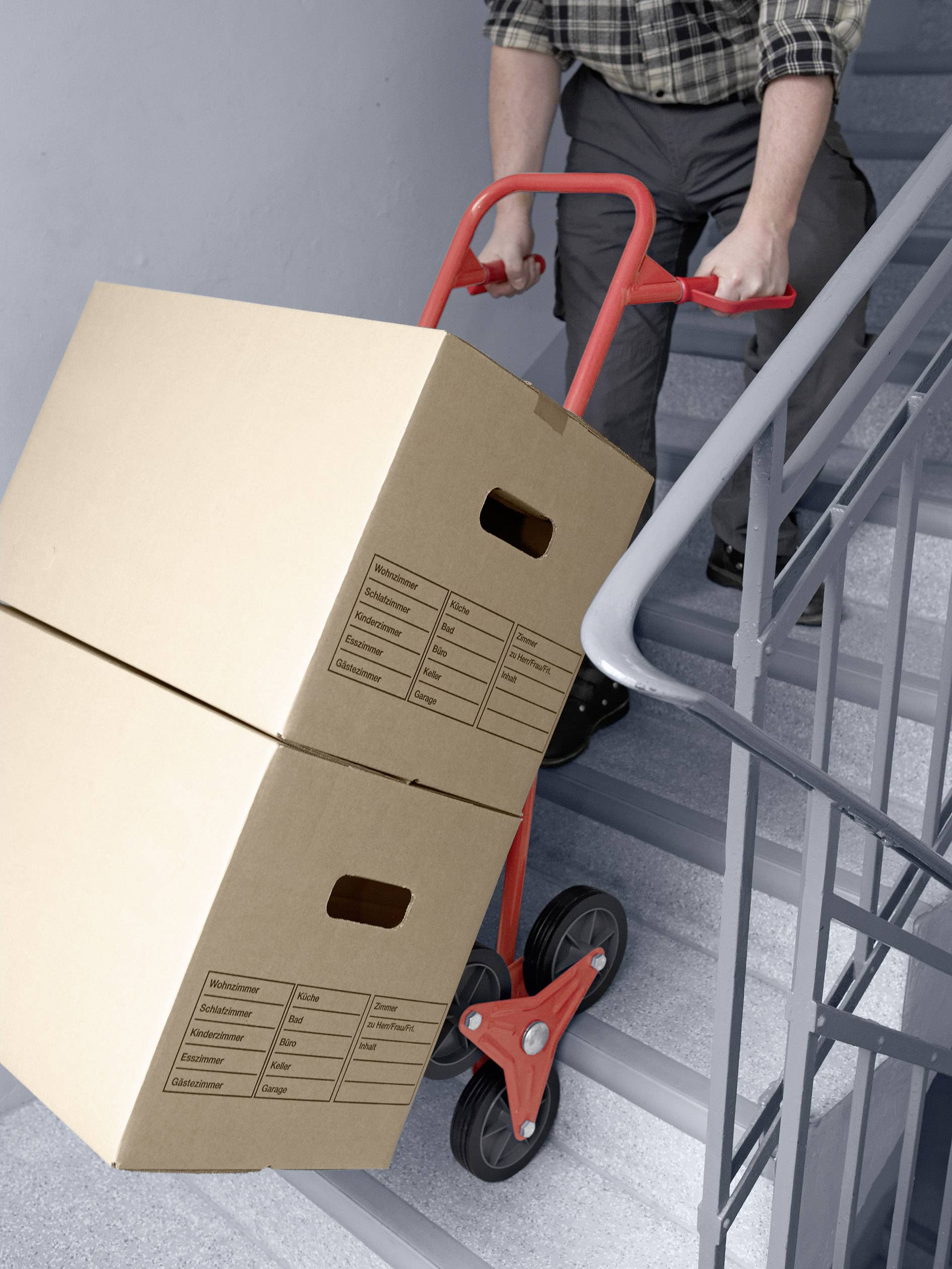 A person is transporting two large boxes down a staircase using a sack barrow.