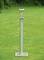 A stainless steel garden light stands on a lawn. The light has a round lampshade and sits on a tall, slender pole.