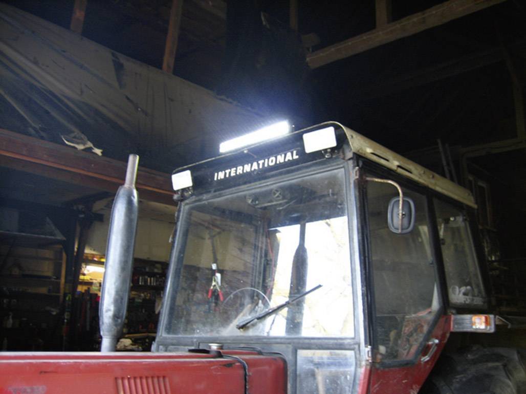 A red tractor stands in a dark barn, with the driver's cabin visible. The word 'INTERNATIONAL' is prominently displayed on the roof.