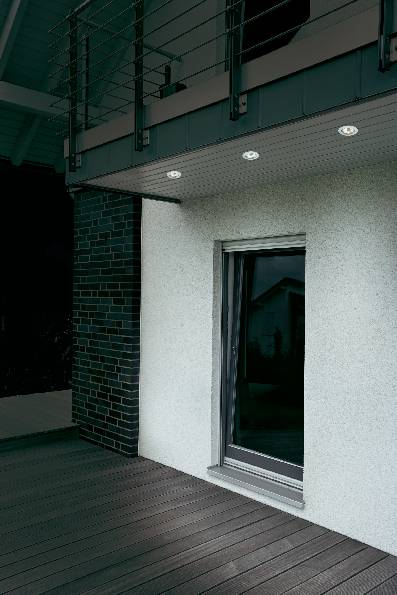 A modern room with wooden flooring, a large window and a patterned wall. On the left, a section with a brick-effect finish is visible.