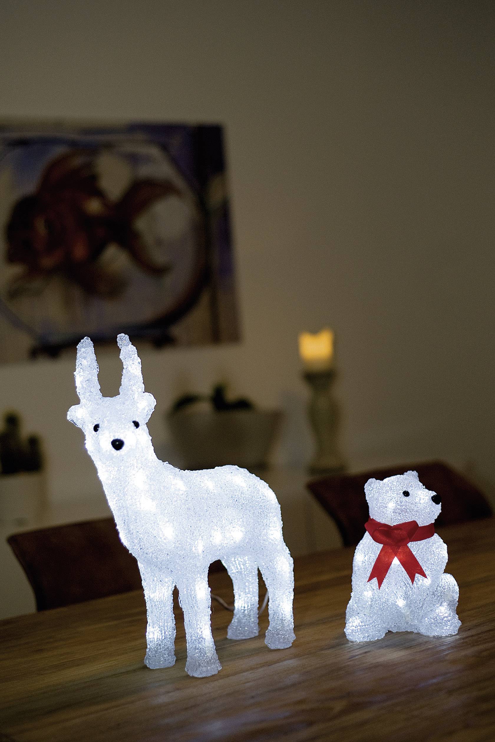 A luminous reindeer and a polar bear with a red bow are standing on a table in a dimmed room, background blurred.