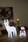 A luminous reindeer and a polar bear with a red bow are standing on a table in a dimmed room, background blurred.