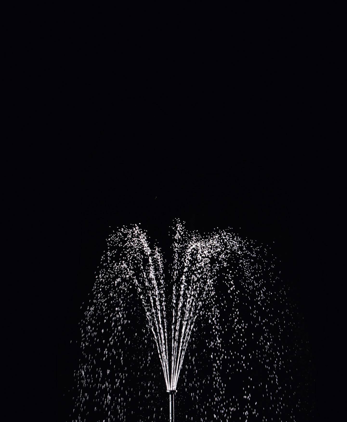 A single fountain sprays water against a pitch-black background, creating a high-contrast and harmonious effect.