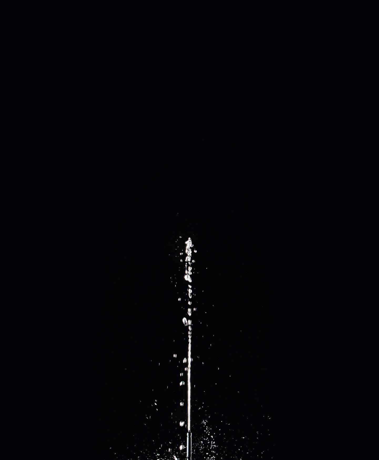 A vertical water fountain sprays in front of a dark background.