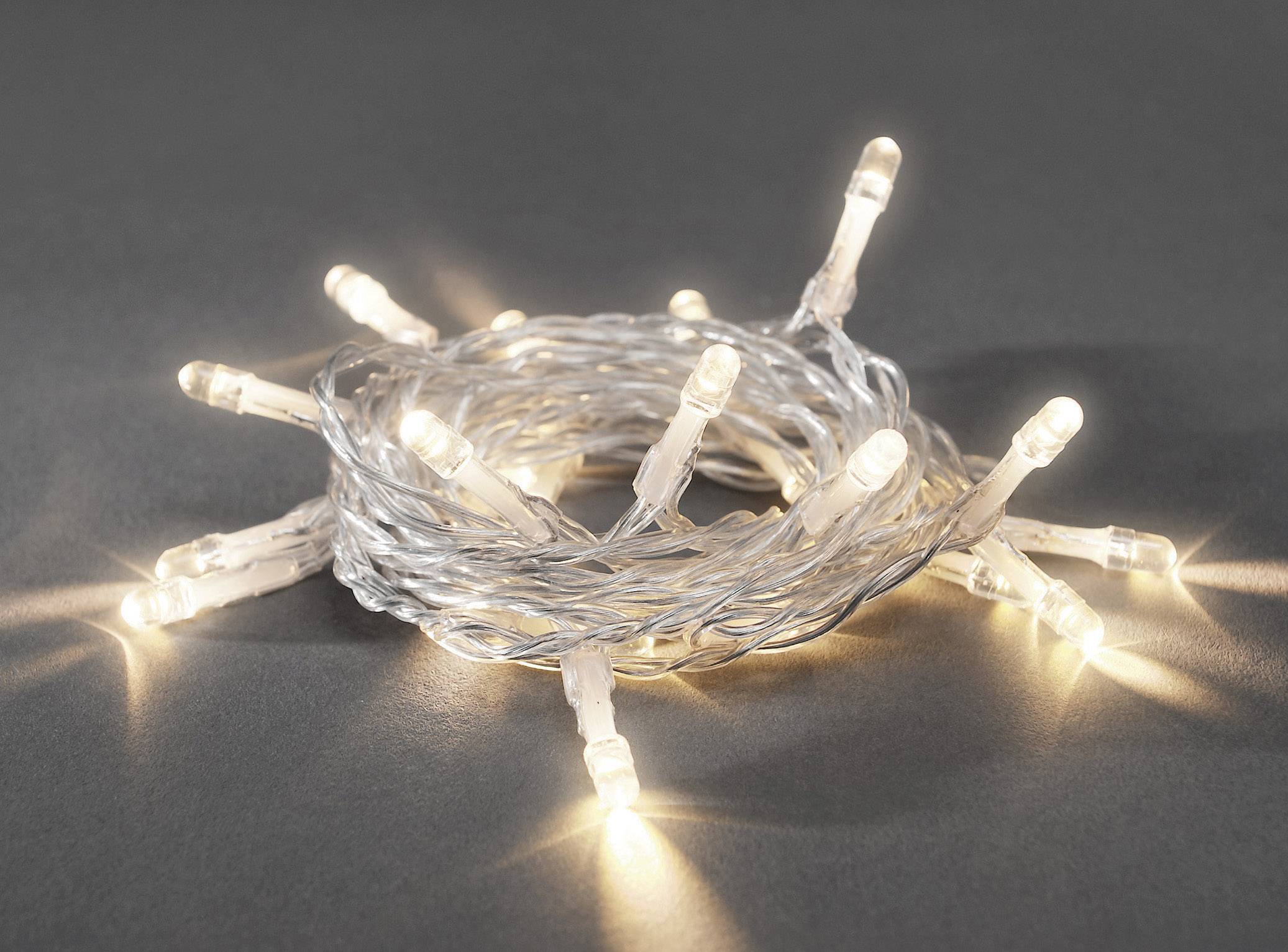 A coiled strand of white LED lights that are illuminated lies on a grey surface, creating a warm light atmosphere.