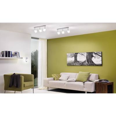 Living room with a green accent wall, white sofa, green armchair, bookshelf and wall art depicting trees. Bright lighting from LED spotlights.