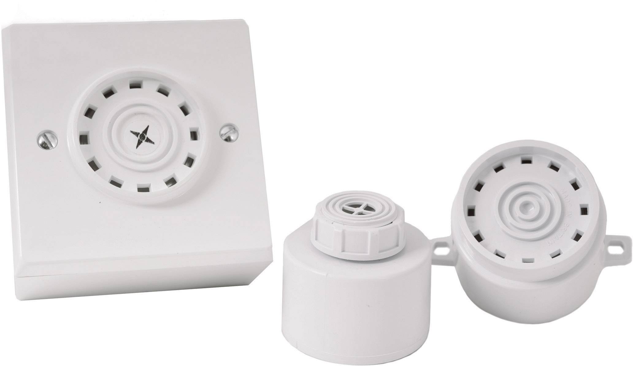 Two white smoke detectors and a white alarm box on a table. All devices are round and have ventilation slots on the top surface.