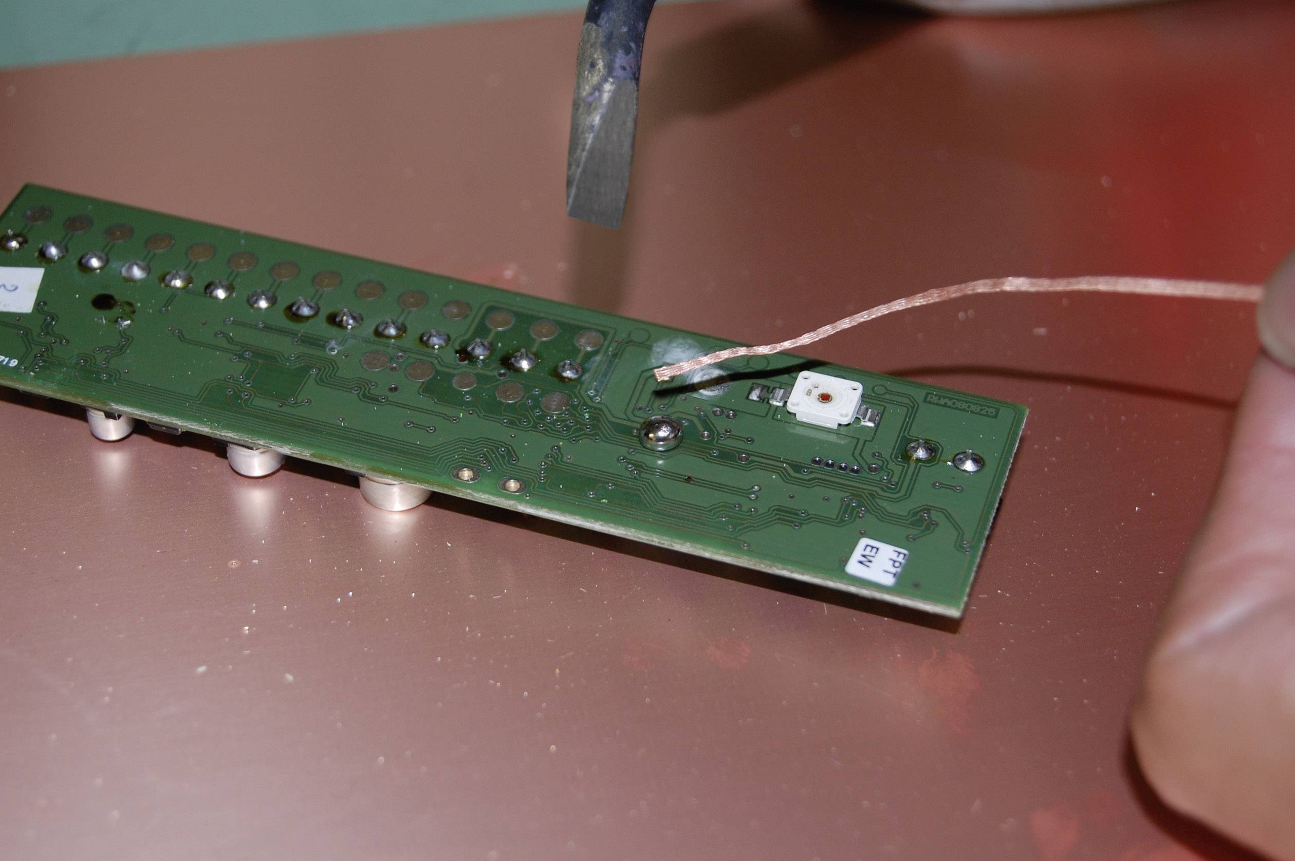 A person is soldering on a green circuit board containing multiple components. The main focus is on the soldering point and the copper wire.