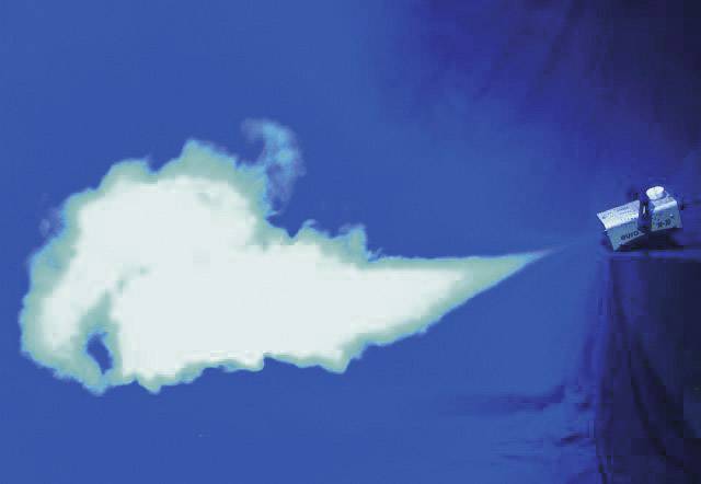A machine is blowing a white plume of smoke onto a blue background, demonstrating the movement and direction of smoke dispersion.