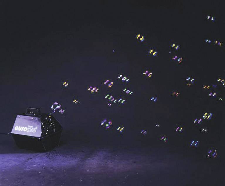 Bubble machine creates shimmering soap bubbles that float vibrantly over a dark background.