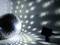 A glitter ball reflects light patterns onto walls and floor in a dark room, while a spotlight illuminates it.
