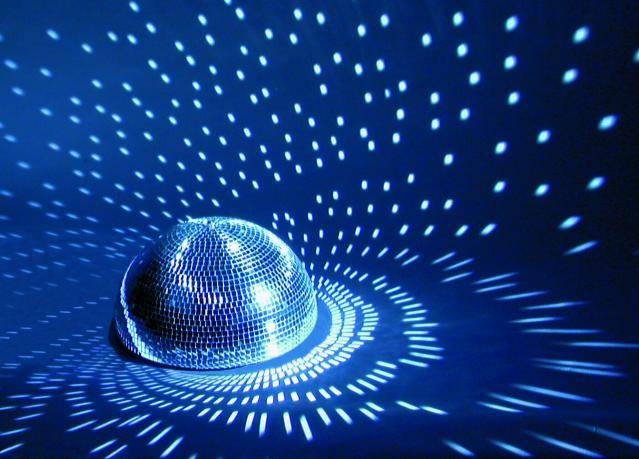 Half-spherical disco ball reflects blue light in a dark room, creating geometric patterns on the walls.