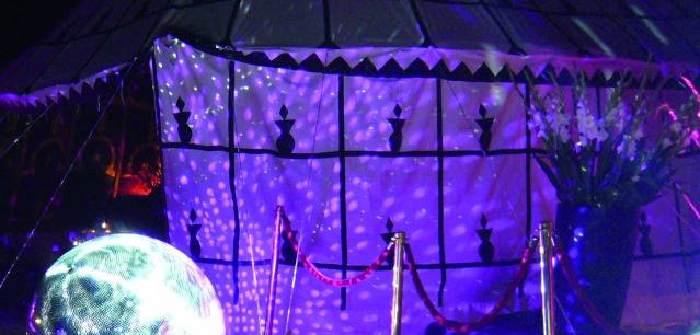 A festive event with colourful lighting. A mirror ball reflects pinpoints of light across a decorated room with curtains.