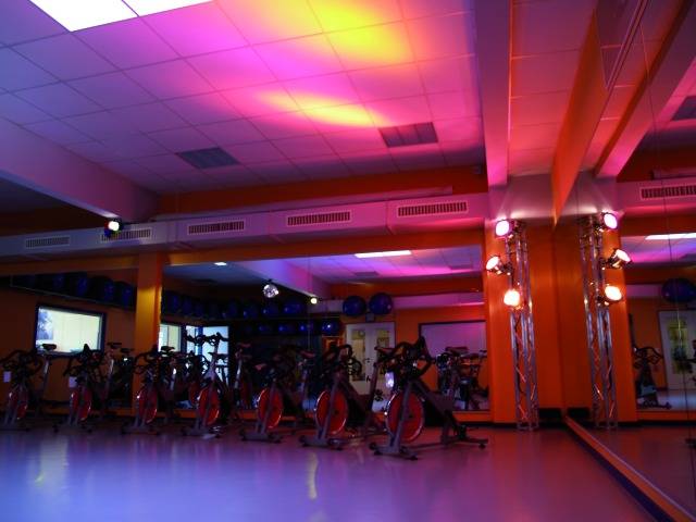 Gym with neon lights. The room is equipped with several stationary bicycles positioned in front of a mirror.