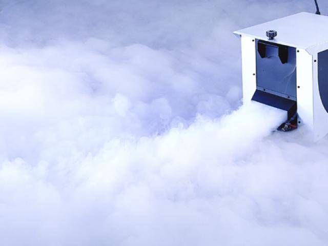A fog machine generates white fog that spreads across the floor. It is white and rectangular in shape.