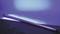 A fluorescent tube glows blue-violet in a dark environment, leaning against a dark surface.