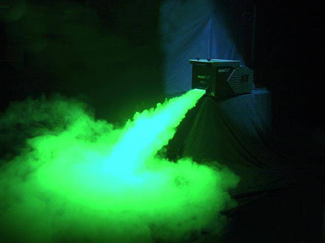 A fog machine generates green mist that spreads forwards. The surroundings are dark, which enhances the light effect.
