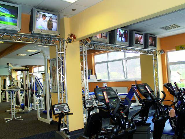 Gym with treadmills and exercise bikes. Several televisions are mounted on the wall, each showing different programmes.
