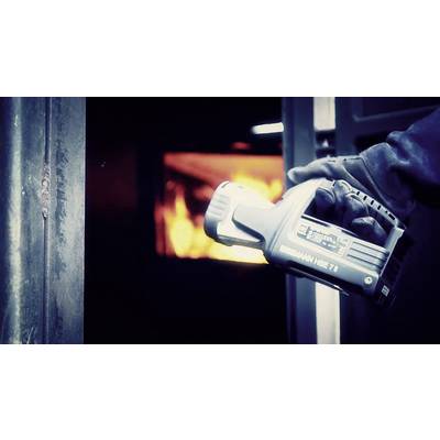 A person is holding an infrared thermometer in front of an open oven with visible flames to measure the temperature.