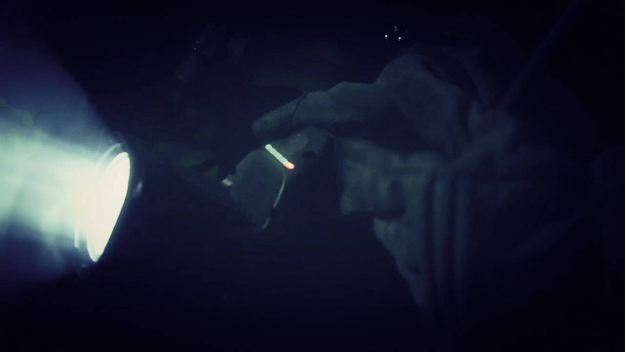 A person is holding a glowing object in the dark, illuminated by a powerful torch on the left side of the image.