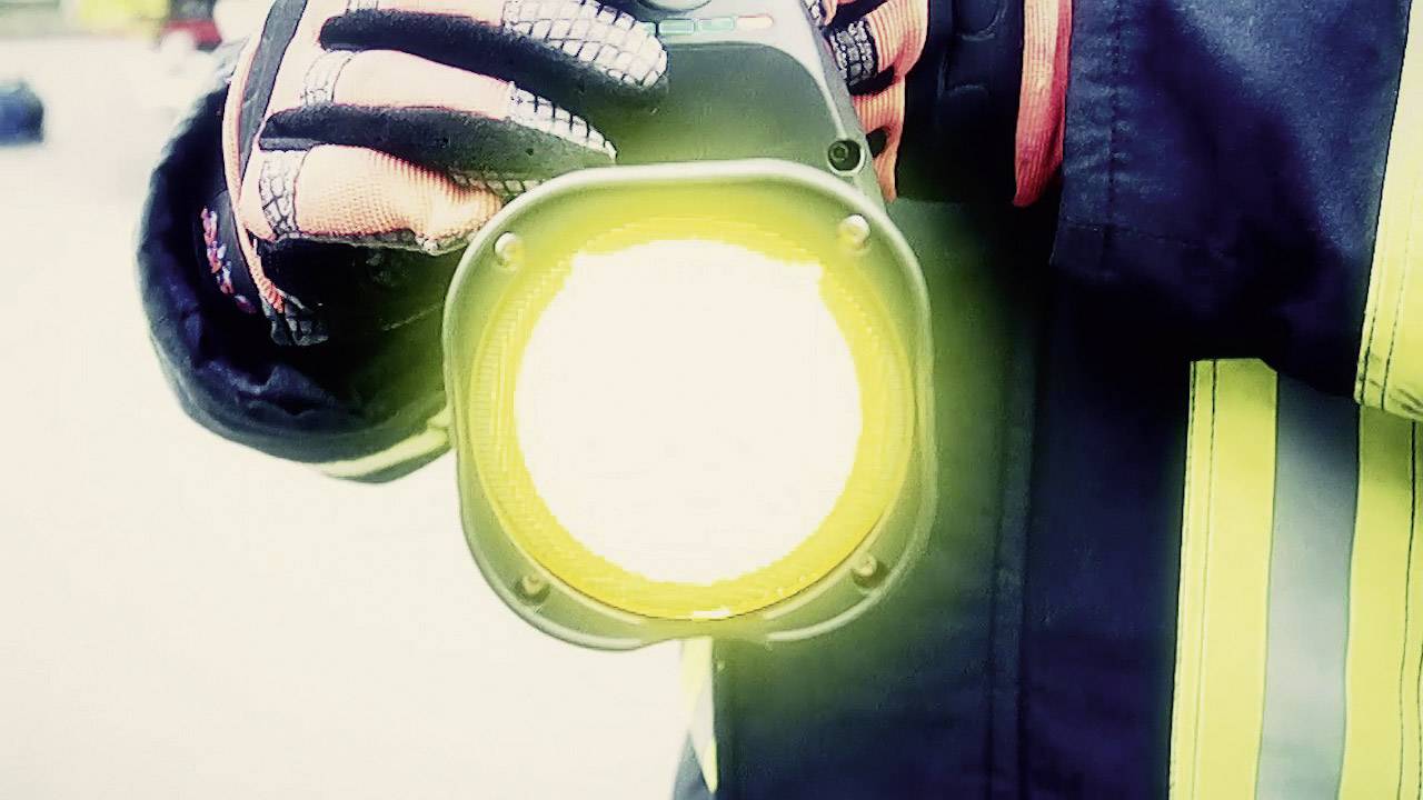 A firefighter is holding a bright torch. The reflective strips on his jacket are visible.