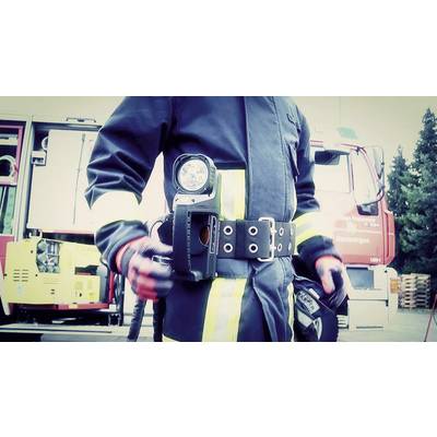 A firefighter in full operational gear stands in front of a fire engine. He has a torch attached to his belt.