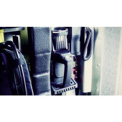 A radio is mounted in a holder on a wall, surrounded by cables and a black bag.