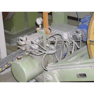 'Industrial machine with hydraulic cylinder and pressure gauge, showing components of a production system. Cables and hoses visible.'